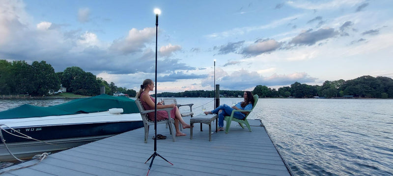 Two ladies sitting in adarondac chairs on a lake dock at dusk while drinking wine. Scene lit by two FLi-PRO telescoping lights.