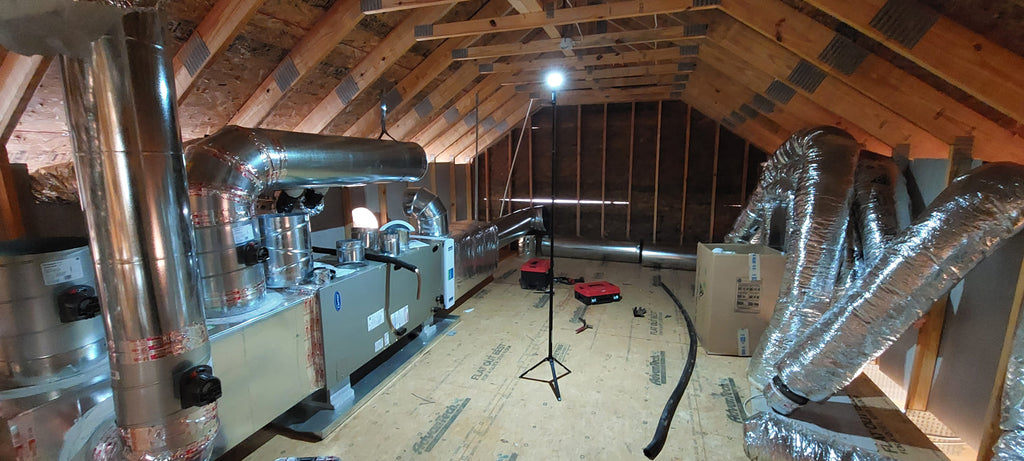 Attic space with insulation and ductwork in a home renovation setting lit up by a FLi-LITE