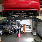 Red car on a lift in a garage with tools and equipment around. Shoplight V2 on the ground lighting up the bay.
