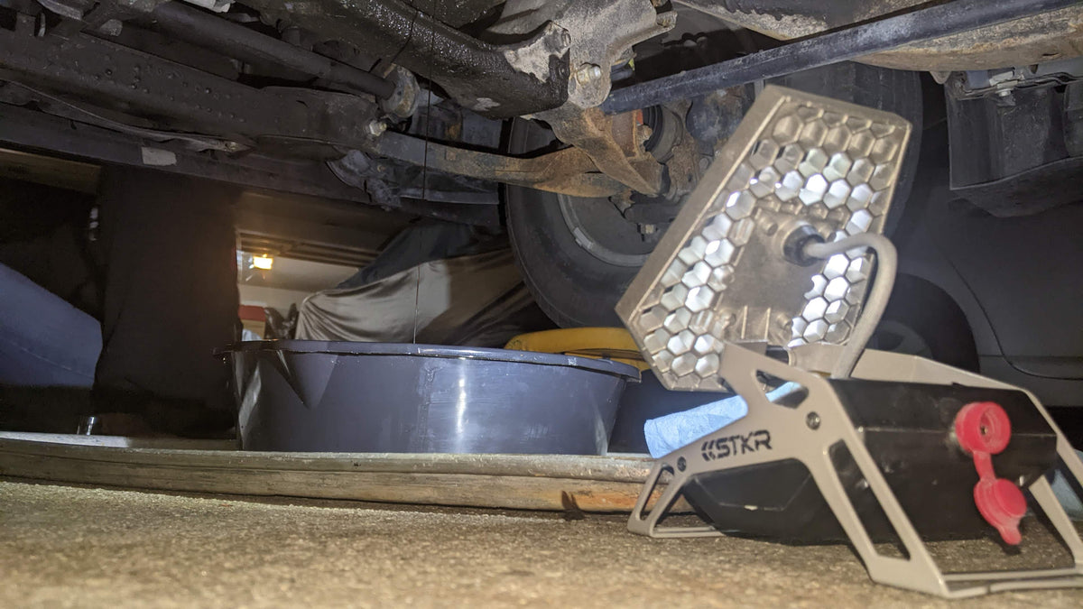 Close-up of a vehicle's undercarriage getting an oil change lit up by a Mobile Task Light