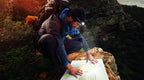 man hiking up in the mountains wearing an STKR headlamp kneeling down and looking at a map on the ground
